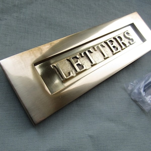 Peut inclure: Une plaque de boîte aux lettres rectangulaire en laiton avec une finition polie, présentant le mot LETTERS en relief en lettres capitales au centre. La plaque comprend un volet articulé et un sachet en plastique contenant la visserie.