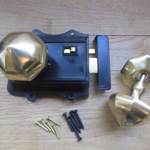 K&ouml;nnte beinhalten: Ein Kastenschloss-Set bestehend aus einem schwarzen, rechteckigen Metallgeh&auml;use mit einem polierten, achteckigen Messingknauf. Ein separater, passender achteckiger Messingknauf mit Vierkantstift, ein Schlie&szlig;blech und kleine Schrauben liegen bei.