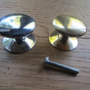 Peut inclure: Deux boutons de placard ronds avec une finition lisse et polie, l'un en métal argenté et l'autre en métal doré, chacun doté d'une large base circulaire et d'une vis de montage en métal positionnée sous les boutons.