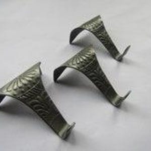 May include: Three dark metallic hooks with a curved, angled design. Each hook features a textured, embossed pattern on the top surface, consisting of radiating lines and leaf-like motifs. The hooks have a pointed end and a wide, flat base.