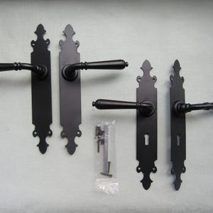 Pode incluir: Quatro maçanetas de porta preto fosco com espelhos alongados e extremidades decorativas pontiagudas. Duas maçanetas são lisas e duas incluem buracos de fechadura. Um pequeno saco plástico contém parafusos e um eixo quadrado.