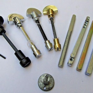May include: A collection of door hardware components including four T-shaped handles with metal shafts, one black knob with a long shaft, a small L-shaped hex key, four straight metal spindles of varying textures, and one circular metal plate.