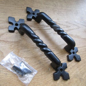 Puede incluir: Dos manijas de puerta de metal negro con un diseño de barra retorcida y placas de montaje en forma de cruz de cuatro puntas en cada extremo. Se incluye una pequeña bolsa de plástico transparente con tornillos de montaje negros.