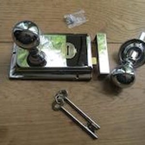 Pode incluir: Um conjunto de fechadura de sobrepor em cromo polido, incluindo um corpo de fechadura retangular com maçaneta redonda, uma maçaneta redonda separada em placa circular, uma chapa testa retangular, duas chaves metálicas e parafusos.