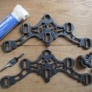 May include: Two dark gray cast iron decorative brackets with intricate cut-out patterns, accompanied by a roll of white cotton sash cord, a metal spike, and two small pulley wheels with attached metal rods for installation and assembly.