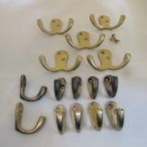 Peut inclure: Un ensemble de quincaillerie métallique comprenant cinq patères doubles à finition dorée, deux crochets simples incurvés et huit petits crochets simples à finition métallique, accompagnés d'une seule petite vis de fixation.