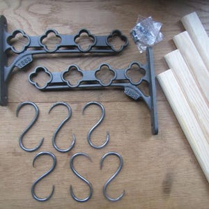Pode incluir: Dois suportes de parede de metal cinza-escuro com um design recortado em forma de trevo e o ano 1883 gravado nos braços, cinco ganchos de metal em forma de S a condizer, quatro varas de madeira clara e um saco com parafusos de montagem.