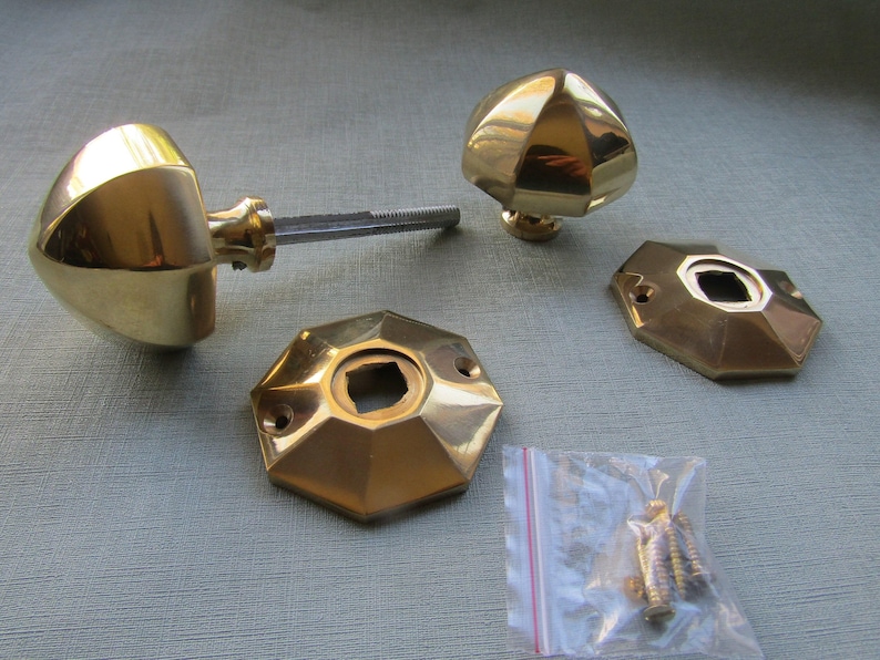 K&ouml;nnte beinhalten: Ein Set aus polierten Messing-T&uuml;rbeschl&auml;gen, bestehend aus zwei facettierten, kuppelf&ouml;rmigen Kn&ouml;pfen, zwei passenden achteckigen Montageplatten mit Schraubl&ouml;chern und einem kleinen Plastikbeutel mit mehreren Metallschrauben.