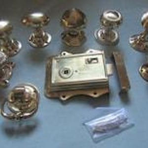 May include: A collection of polished brass door hardware including seven round door knobs, one oval door knob, one ring-style door knocker, a rectangular mortise lock box with a central square spindle hole, and a small plastic bag containing screws.