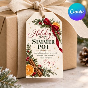 Op de afbeelding: Een rechthoekig cadeaulabel met een crèmekleurige achtergrond, voorzien van een rood lint, groene dennentakken, kaneelstokjes en schijfjes sinaasappel. De tekst luidt Holiday SIMMER POT, Add all ingredients to a crock pot and keep on low & smell all winter, Enjoy.
