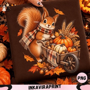 May include: A brown fabric square featuring a graphic illustration of a squirrel wearing a plaid scarf, pushing a wooden wheelbarrow filled with pumpkins, wheat stalks, and acorns, surrounded by scattered orange and yellow autumn leaves.