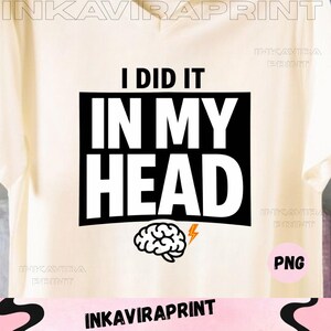 Può includere: T-shirt color crema con una grafica rettangolare nera che recita "I DID IT IN MY HEAD" in lettere bianche in grassetto. Sotto il testo c'è un'illustrazione di un cervello con un fulmine. La maglietta è a collo a V.