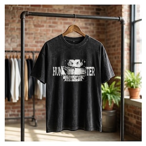 May include: A black acid-wash t-shirt featuring a graphic print of three anime character eyes stacked vertically within a rectangular frame, with the text HUNTER printed in a distressed white font across the centre of the design.