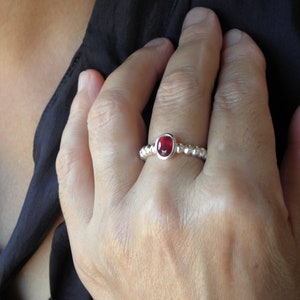 Pode incluir: Um anel de prata com uma pedra preciosa vermelha engastada em uma banda de contas.
