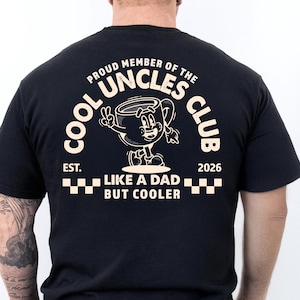 May include: Black t-shirt with a white graphic of a cartoon coffee cup giving a peace sign. The text reads "COOL UNCLES CLUB" and "LIKE A DAD BUT COOLER". The shirt also has the text "EST. 2026".