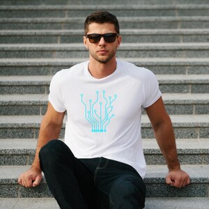 Pu&ograve; includere: T-shirt bianco con un design a circuito stampato azzurro. La maglietta &egrave; a maniche corte e ha un girocollo. La persona nell'immagine indossa occhiali da sole e jeans blu scuro. Lo sfondo &egrave; una scala di cemento.