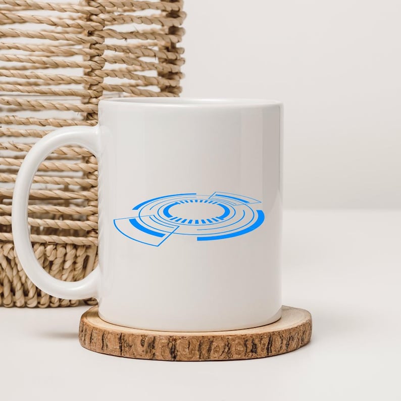 Pu&ograve; includere: Tazza in ceramica bianca con un design tecnologico circolare blu. La tazza &egrave; appoggiata su un sottobicchiere rotondo in legno. Il manico &egrave; a sinistra. Sullo sfondo un cesto intrecciato.
