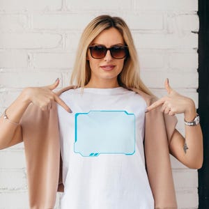 Pu&ograve; includere: T-shirt bianco con grafica rettangolare azzurra dal design futuristico. La grafica ha un bordo azzurro. La persona nell'immagine indossa occhiali da sole e una giacca beige.