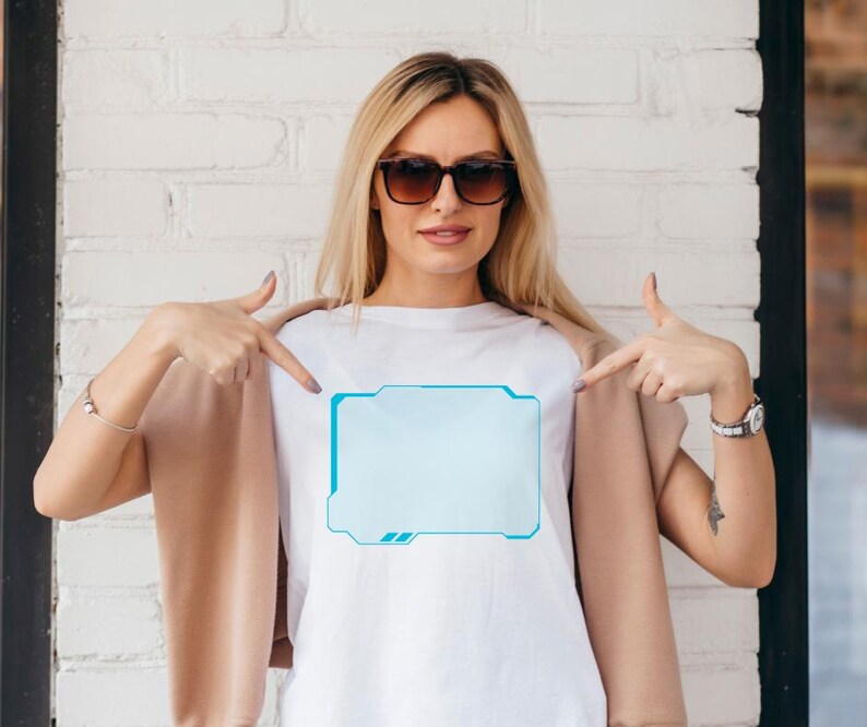 Pu&ograve; includere: T-shirt bianco con grafica rettangolare azzurra dal design futuristico. La grafica ha un bordo azzurro. La persona nell'immagine indossa occhiali da sole e una giacca beige.