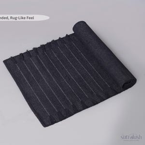 May include: A rolled-up, dark blue rug with a textured surface and vertical white stripes. The rug has a fringed edge and the text "Grounded, Rug-Like Feel" is in the upper left corner. The SutraLush logo is in the lower right corner.