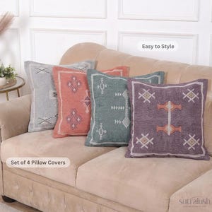 May include: Set of four decorative pillow covers in shades of gray, coral, teal, and purple. Each pillow features a geometric design in white and orange. The pillows are arranged on a beige sofa. The text "Easy to Style" and "Set of 4 Pillow Covers" are visible.