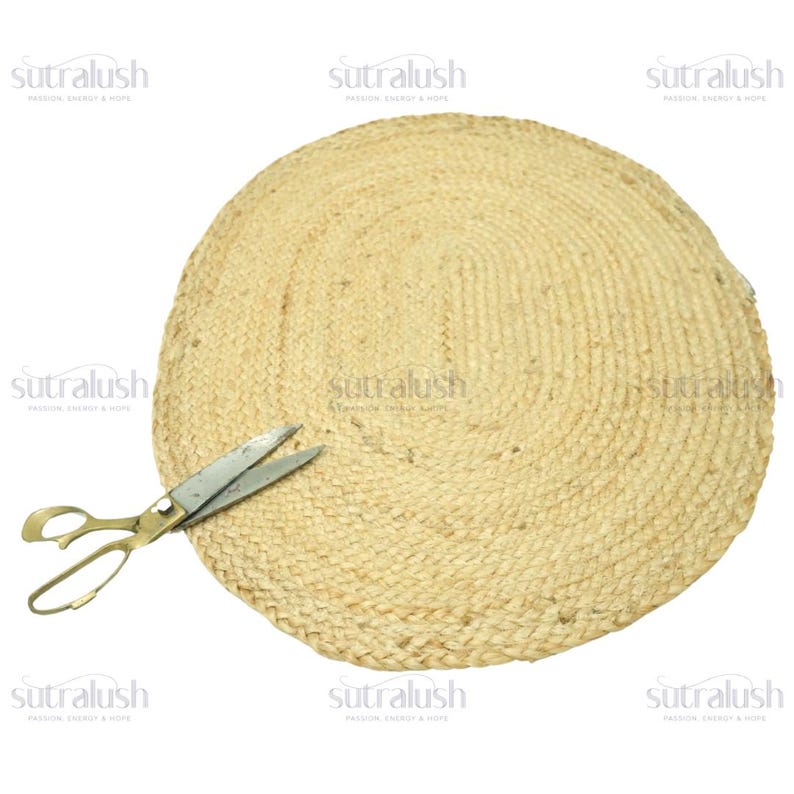 May include: A round, woven jute placemat with a natural tan color. A pair of vintage-style scissors rests on the edge of the placemat. The placemat is made of a thick, durable material and is suitable for home decor.