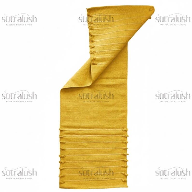 May include: Mustard yellow rectangular rug with horizontal white stripes and fringe detailing. The rug is partially folded, revealing its texture. The brand name "sutralush" is printed on the rug.