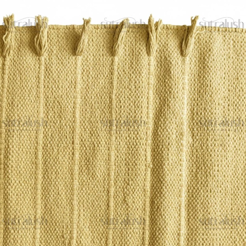 May include: Close-up of a textured, woven fabric in a light yellow color. The fabric has vertical stripes and knotted fringe along the top edge. The weave is tight, creating a durable and visually appealing textile.