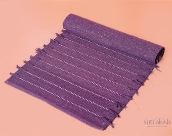 Peut inclure: Un tapis violet tissé enroulé, avec des rayures blanches et des bords effilochés. Le tapis est fait d'un tissu texturé et est présenté sur une surface couleur pêche. C'est un article de décoration intérieure.
