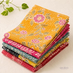 May include: A stack of five folded rectangular cotton quilts featuring intricate kantha stitching. The top quilt is mustard yellow with a pink and green floral pattern. Beneath it are layers in shades of magenta, teal, black, and red with floral prints.