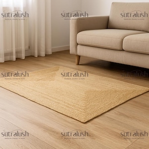 May include: A rectangular, beige jute rug with a woven texture. The rug is placed on a light-colored wooden floor, with a beige sofa in the background. The rug has a border design.