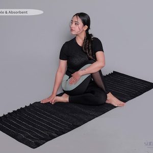 Op de afbeelding: Een zwarte yogamat met een getextureerd oppervlak en franjes aan de randen. De mat bevat de tekst "Breathable & Absorbent" in de linkerbovenhoek en het "sutralush"-logo in de rechterbenedenhoek, op een neutrale grijze achtergrond.