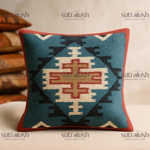 May include: Square decorative pillow with a geometric pattern in teal, black, cream, and red. The pillow has a red border and features a central cross-like design. The text "sutralush" is visible in the corners.