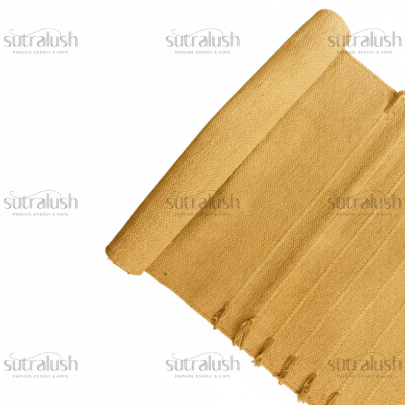 May include: A rolled-up, mustard-yellow woven rug with a textured surface. The rug has vertical stripes and a fringe detail along one edge. The brand name "sutralush" is printed in white in multiple places.