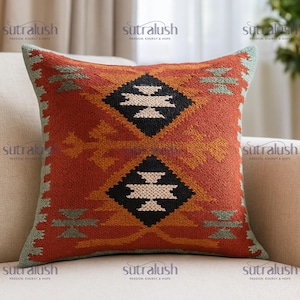 May include: Square decorative pillow with a geometric pattern in shades of orange, black, white, and green. The pillow has a textured appearance and is placed on a neutral-colored surface. The text "sutralush" is visible on the pillow.