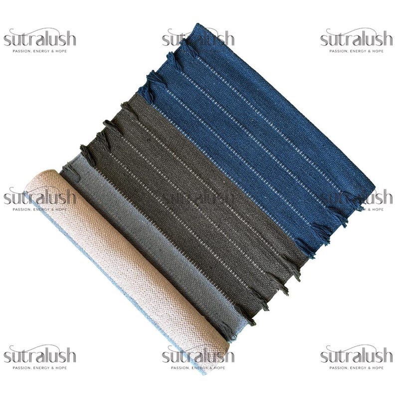 Peut inclure: Quatre tapis rectangulaires tiss&eacute;s, enroul&eacute;s et d&eacute;roul&eacute;s, dans des tons beige, gris et bleu. Chaque tapis pr&eacute;sente des rayures verticales blanches et des bords frang&eacute;s. Les tapis sont dispos&eacute;s en diagonale, mettant en valeur leurs couleurs et textures vari&eacute;es.
