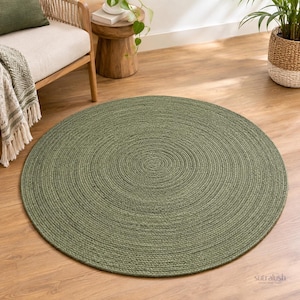 May include: A round, sage green area rug featuring a braided, coiled texture. The rug is constructed from thick, woven fibers arranged in a continuous circular pattern, creating a uniform, dense surface that lies flat on the floor.