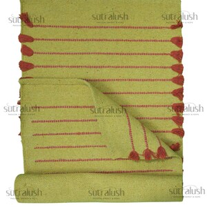 May include: A folded, light green woven rug with horizontal red stripes and red tassels along one edge. The rug is rolled up at the bottom, revealing the underside. The text "sutralush" is printed on the rug.