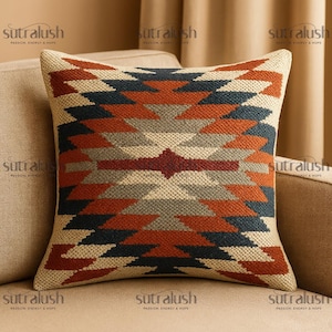 May include: Square decorative pillow with a geometric pattern in shades of rust, navy, gray, and cream. The pillow is placed on a beige sofa. The brand name "sutralush" is printed on the pillow.