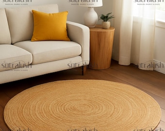 Puede incluir: Una alfombra redonda de yute marrón dorado con un diseño en espiral sobre un suelo de madera. Un sofá crema con un cojín amarillo está en el fondo, junto a una mesa auxiliar de madera y una lámpara blanca.