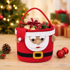 May include: A red rope storage basket designed to resemble Santa Claus, featuring a white rope beard, a black belt with a yellow buckle, and a red handle. The basket is filled with Christmas ornaments, pine sprigs, and wrapped gift boxes.