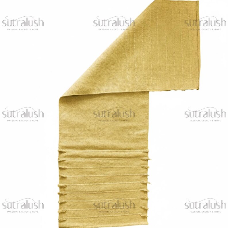 May include: A folded, golden-yellow textile with a textured surface and fringed edges. The text "sutralush PASSION ENERGY & HOPE" is printed on the fabric. The textile is likely a scarf or wrap.