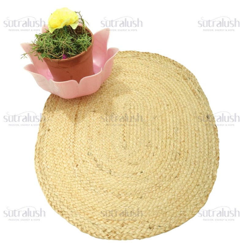 May include: A round, natural jute rug with a woven texture. A small potted plant with green foliage and a yellow flower sits in a pink, lotus-shaped planter. The rug is beige and the planter is pink.