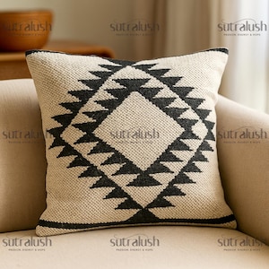 May include: Square beige throw pillow with a geometric black pattern. The design features a diamond shape with triangles. The pillow has a textured appearance and a black border. The text "sutralush" is printed on the pillow.