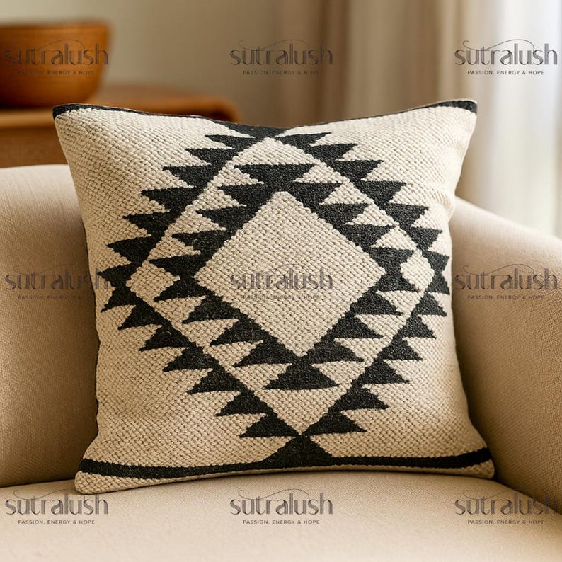 May include: Square beige throw pillow with a geometric black pattern. The design features a diamond shape with triangles. The pillow has a textured appearance and a black border. The text "sutralush" is printed on the pillow.