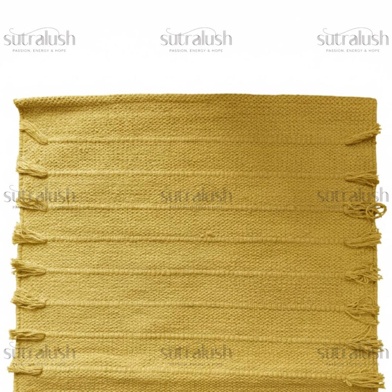 May include: Mustard yellow woven rug with horizontal stripes and fringe detailing. The rug has a textured appearance and is rectangular in shape. The rug is a home decor item, suitable for living rooms or bedrooms.