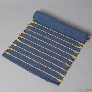 May include: A rolled-up blue rug with yellow stripes and tassels. The rug is made of woven fabric and has a rectangular shape. The stripes run lengthwise across the rug.