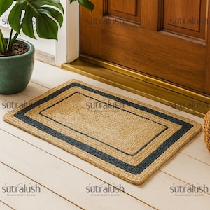 May include: Rectangular jute doormat with a dark blue border. The mat is made of woven natural fibers and is placed in front of a wooden door. The doormat measures approximately 30 inches long and 20 inches wide.