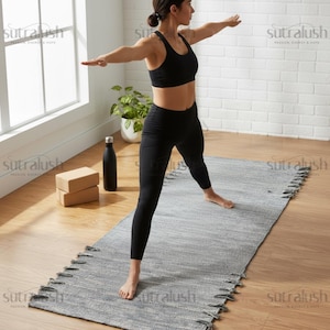 May include: A person in black activewear practices yoga on a grey and white woven yoga mat. A black water bottle and two tan yoga blocks are visible. The yoga mat has a fringe detail on the edges. The word "sutralush" is printed on the image.