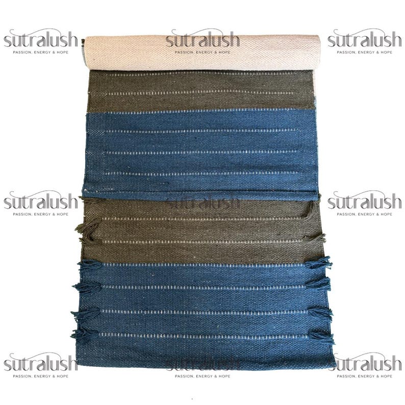 Peut inclure: Un tapis &agrave; rayures enroul&eacute;, avec une section sup&eacute;rieure beige, passant &agrave; des rayures vert olive et bleues. Le tapis a des lignes blanches et des franges sur le bord inf&eacute;rieur. Le nom de la marque "sutralush" est imprim&eacute;.